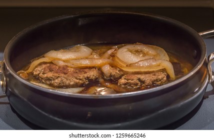 Turkey Salisbury Steak:  Turkey Salisbury Steak Topped With Sauteed Onions And Cooked In A Large Pan On Top Of The Stove.