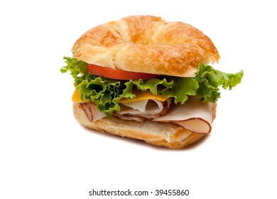 A Turkey Sandwich On A Croissant With Lettuce, Cheese And Tomatoes On A White Background