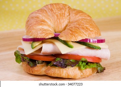 Turkey Sandwich On A Croissant With Swiss Cheese, Avocado, Tomatoes, Lettuce, And Onion.