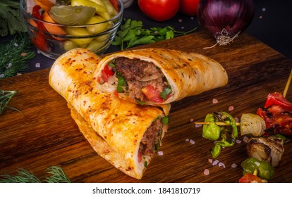 Turkish and Arabic Traditional Ramadan Adana Kebab Roll Wrap serving with yogurt, aubergine salad and hot pepper pickles on rustic wooden background. 