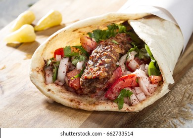 Türkisches und arabisches Traditionelles Ramadan Adana Kebab Roll Wrap mit Jogurt, Auberginensalat und scharfen Pfefferpflücken auf rustikalem Holzhintergrund. 