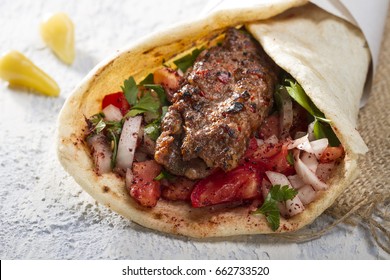 Türkisches und arabisches Traditionelles Ramadan Adana Kebab Roll Wrap mit Jogurt, Auberginensalat und scharfen Pfefferpflücken auf rustikalem Holzhintergrund. 