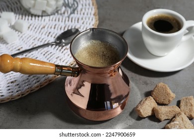 Turkish coffee. Cezve and cup with hot aromatic coffee and sugar on grey table