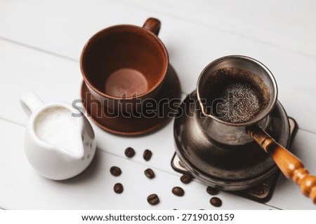 Turkish coffee in cezve with empty ceramic cup, milk pitcher and coffee beans on white rustic table