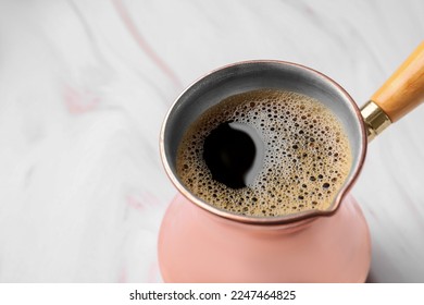 Turkish coffee in cezve on white marble table, closeup. Space for text