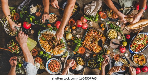 Turkish cuisine family feast. Flat-lay of peoples hands and lamb chops with quince, beans, salad, babaganush, rice pilav, pumpkin dessert, lemonade over rustic table, top view. Middle East cuisine