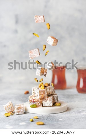 Turkish delight levitation flying photo. Sweet Lokum with pistachio nuts and tea cups. Vertical food photo. Creative concept 