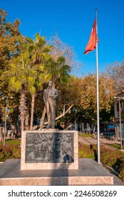 Turkish flag by bronze Ataturk monument statue on carved structure with lush trees and clear blue sky in the background during sunny day