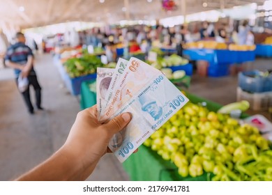 Turkish Lira Banknotes In Hand Against The Background Of Vegetables At The Farmer's Market. The Concept Of Consumer Economy And Inflation Of The National Currency Of Turkey.