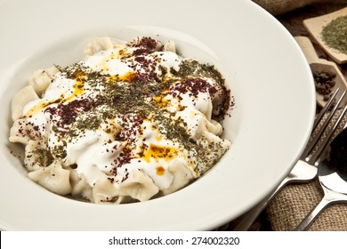 Türkisches Manti Manlama auf Teller mit rotem Pfeffer, Tomatensoße, Jogurt und Minze