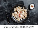 Turkish manti with yoghurt and tomato sauce in a plate. Black background. Top view.