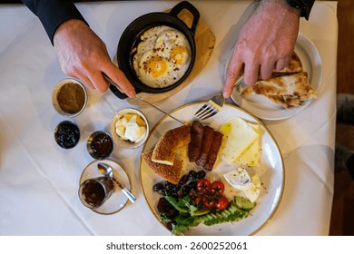 Desayuno de estilo turco o mediterráneo. Desayuno turco. Variedad de verduras frescas, aceitunas, quesos, mermeladas y untables en platos Pequeños sobre una mesa cubierta de mantel blanco. Hombre irreconocible 