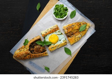 Turkish pide or Turkish pizza flat bread and pointed at both ends filled with minced meat and toped with veges, cheese and egg or different combination. black background empty space for text.