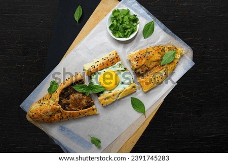 Turkish pide or Turkish pizza flat bread and pointed at both ends filled with minced meat and toped with veges, cheese and egg or different combination. black background empty space for text.