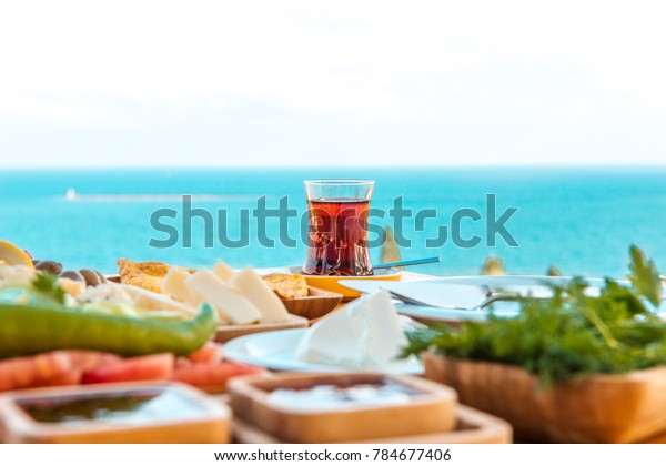 Turkish tea with breakfast on the table in front\
of sea background landscape at Summer season. Turkish or Greek\
Breakfast at seaside. This turkish tea is red. Holiday and vacation\
in Turkey or Greece
