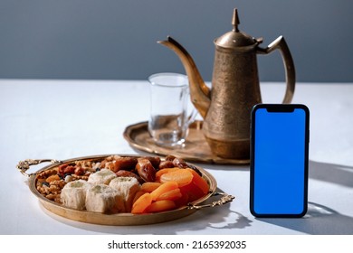 Turkish tea and sweets, smartphone with blue chroma key screen, hot drink in traditional armudu glass close-up. National islamic pastry, treats.