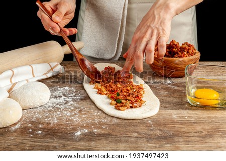 A Turkish woman is preparing kiymali pide, traditional flatbread with ground meat paste onto flattened dough and egg is spread on top of the mixture before baking in brick oven.