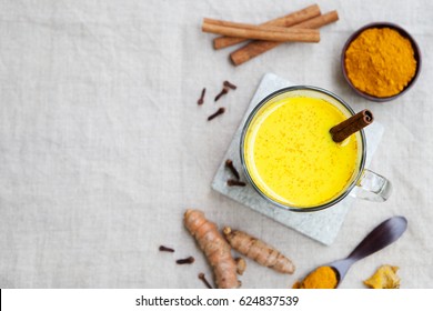 Turmeric drink, latte, tea, milk with cinnamon in a glass mug with fresh and dried turmeric on a textile grey background. Top view. Copy space.