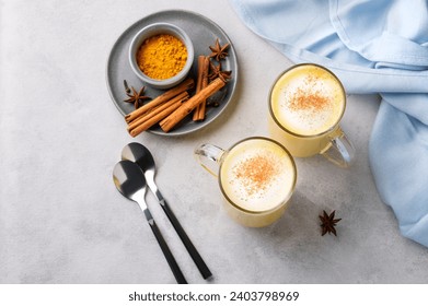 Turmeric golden milk latte with spices and honey. Detox, immunity boosting, anti-inflammatory, healthy, cozy drink in a glass cup on a light background with blue napkin. Top view. - Powered by Shutterstock