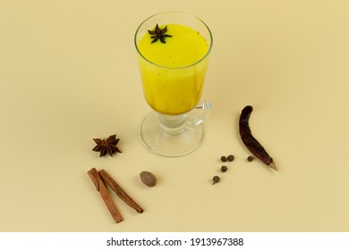 Turmeric latte with cinnamon sticks and anise herb on light-yellow background. Immunity boosters concept. Alternative coffee.