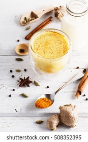 Turmeric latte and spices over white wooden background close up