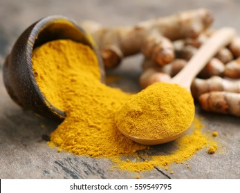 Turmeric powder and fresh turmeric on wooden background.