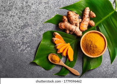 Turmeric powder and fresh turmeric root on grey concrete background with copyspace. Spice, natural coloring, alternative medicine.