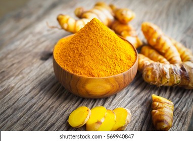 Turmeric powder and fresh turemric in wood bowls on wooden table. Herbs are native to Southeast Asia.