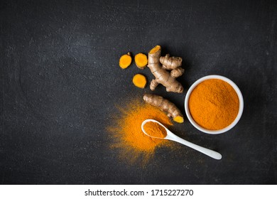 turmeric powder in white bowl with spoon and turmeric slices on black cement background , top view , flat lay.