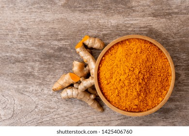 Turmeric Powder In Wooden Bowl And Tumeric Root Isolated On Rustic Wood Table Background. Top View.  