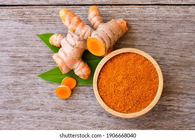 Turmeric powder in wooden bowl with tumeric rhizome and tumeric sliced isolated on old wood table background. Top view. Flat lay.