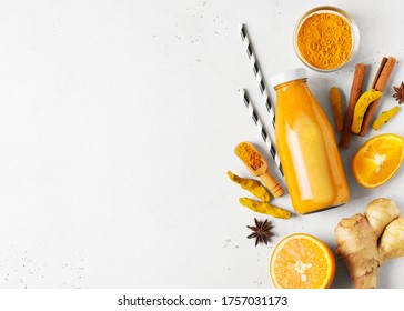Turmeric smoothie in glass bottle with ingredients, turmeric powder, ginger and spice on white or light grey background, copy space, flat lay, top view