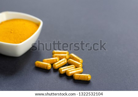 Turmeric yellow powder in a white bowl and capsules on dark background with copy space. Healthy spice.
