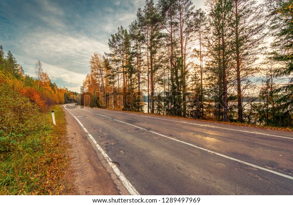 Turn the country broken road. Mixed\
forest. Sunset over the forest lake. Autumn weather. Beautiful\
nature. Russia, Europe. View from the side of the\
road.
