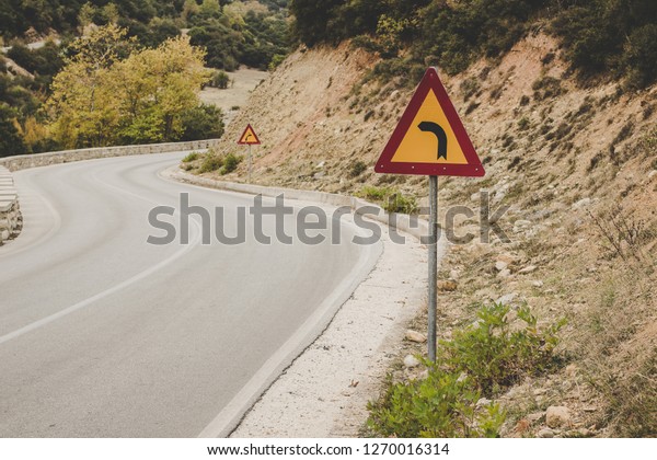 turn left sign on empty curved car\
road in highland mountain rocky country\
environment