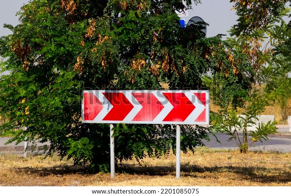 Turn road traffic direction white arrows red\
background sign in front of a\
tree