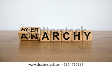Turned a cube and changed the word 'anarchy' to 'hierarchy'. Beautiful wooden table, white background. Business concept. Copy space.