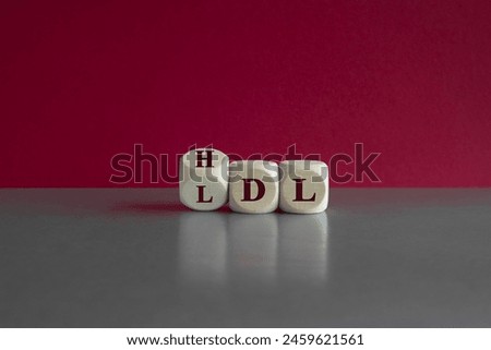 Turned a cube and changes the expression LDL (low density lipoprotein) to HDL (high density lipoprotein). Beautiful red background, grey table. Medical concept. Copy space.