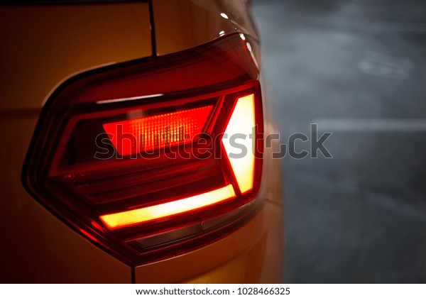 Turned on red led\
taillight on orange car hatchback parked in underground parking lot\
with concrete floor