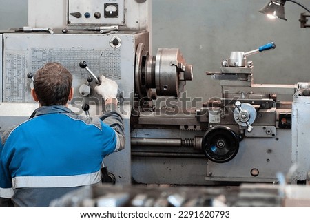 Turner at lathe in workplace. View of worker from back. Metal processing in lathe shop. Equipment adjuster..