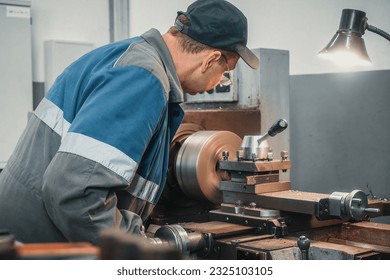 A turner in overalls works on a lathe in a workshop in a factory. Authentic workflow. Back view. A man melts a detail on a machine. - Powered by Shutterstock