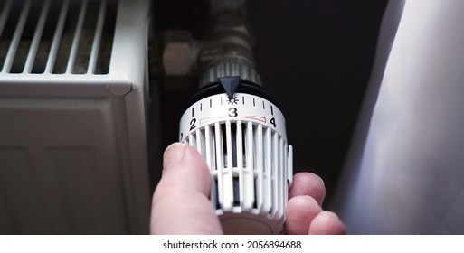 turning down thermostat on radiator to save energy due to heating cost price hike - Shutterstock ID 2056894688