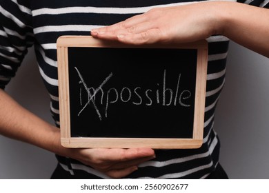 Turning the impossible into the possible. Impossible written with white chalk on a blackboard in woman's hands. Motivation for success, away with doubts - Powered by Shutterstock