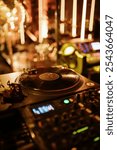 A turntable playing a vinyl record at a nightclub. The scene is illuminated by warm, golden lights, creating a vibrant atmosphere. The setup highlights the DJ