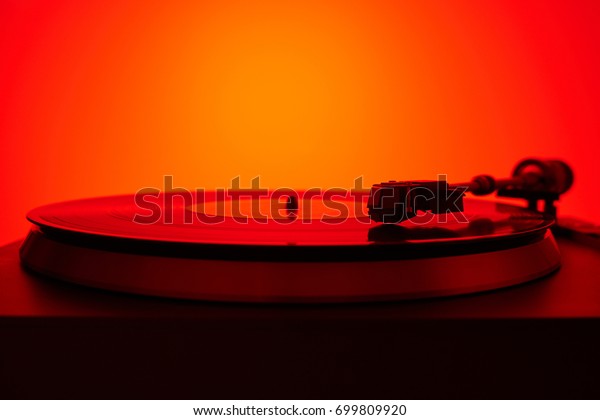 Turntable vinyl record player in the red light. Retro\
audio equipment for disc jockey. Sound technology for DJ to mix\
& play music. Black vinyl record. Vintage vinyl record player\
in the red light  