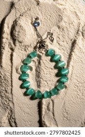 Turquoise beaded bracelet with silver chain and crystal charm placed on a textured white powder surface with directional lighting.