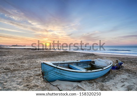 Turquoise blue fishing boat at sunrise on Bournemouth beach with pier in far distance