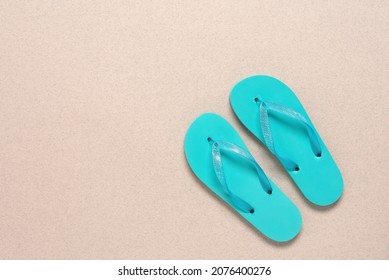 Turquoise blue flip flops. Beige paper background with splashes. Summer vacation concept. Top view, flat lay. Textured object, selective focus