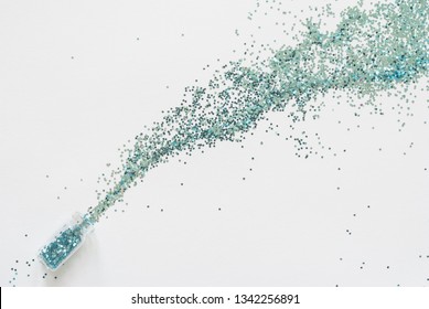 Turquoise Blue Glitter  Confetti Spill Out Of A Small Glass Jar Diagonally On A White Paper Background.