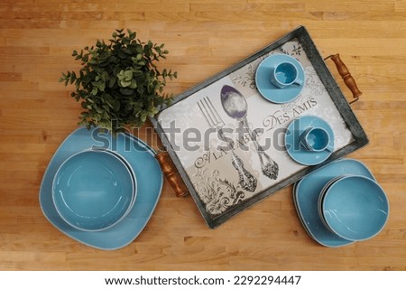 turquoise blue tableware with a green plant and a tray on a wooden table. Translation on the tray: at the table with friends